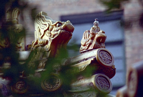 CHINA, Shandong, Qufu, Close up of decorative roof carvings in the ancient grounds where Confucius practiced seen through leaves