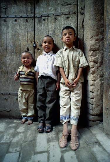 CHINA, Xinjiang, Kashgar, Three young boys standing against a wooden door on a cobbled street