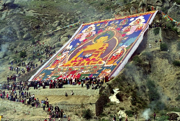 CHINA, Tibet, Drepung Monastery, Parade toward the Thangka and onlookers at a silken Thangka Buddhist ceremony for the cycle of life with massive brightly colourd hillside Buddha image