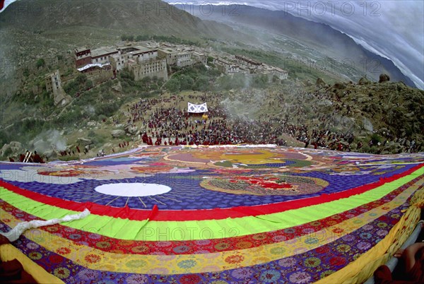 CHINA, Tibet, Drepung Monastery, Wide angled view looking down massive colourful image of buddha to Parade toward the Thangka with onlookers at a silken Thangka Buddhist ceremony for the cycle of life