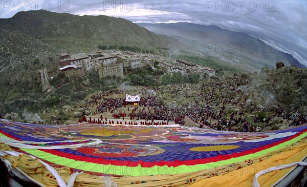 CHINA, Tibet, Drepung Monastery, Wide angled view looking down massive colourful image of buddha to Parade toward the Thangka with onlookers at a silken Thangka Buddhist ceremony for the cycle of life