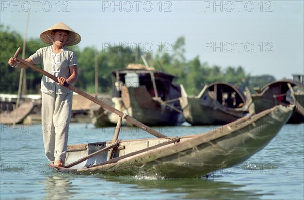 VIETNAM, Central, Hue, Local transport woman standing on the edge of her canoe rowing with a single oar.