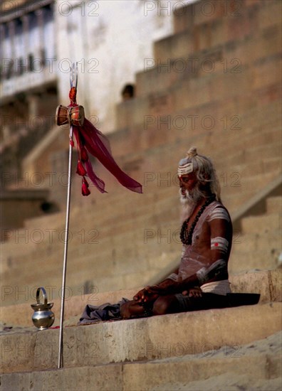 INDIA, Uttar Pradesh, Varanasi, Sadhu meditating in the early morning sun on the ghats of the River Ganges