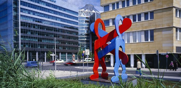 GERMANY, Berlin, Red and blue sculpture by Keith Haring entitled Boxers with city road and architecture behind