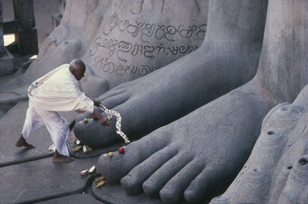 INDIA, Karnataka, Sravanabelagola, "Jain puja at feet of seventeen metre high naked statue of Bahubali, the Gomateshvara.  One of the oldest and most important Jain pilgrimage centres in India. "