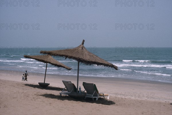 GAMBIA, People, Hotel beach front with woman and child walking hand in hand over sand. Sun loungers and parasols in the foreground