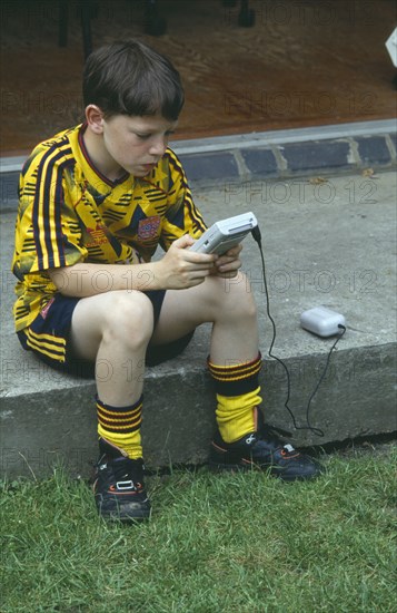 CHILDREN, Play, Computer Games, Young boy in a football kit playing a Nintendo Gameboy