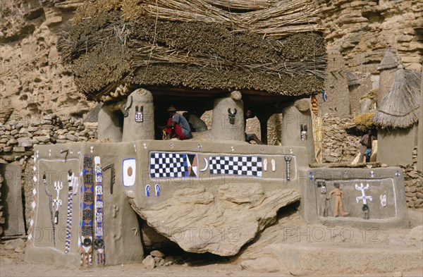 MALI, Bandiagara Cliffs, Newly painted Dogon Toguna or meeting place with men sitting on raised floor between pillars supporting thick millet thatched roof.