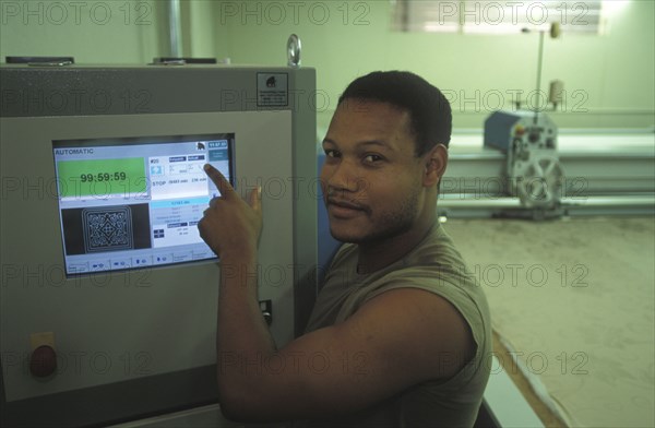 SOUTH AFRICA, Western Cape, Cape Town, Worker setting up automatic fabric cutting machine at Pre Les bedroom textiles factory