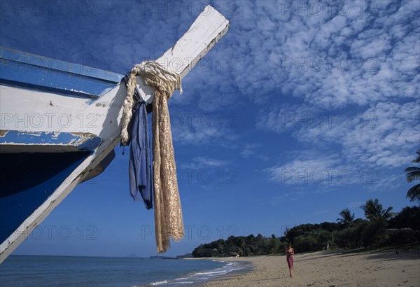 THAILAND, Krabi, Koh Lanta, Relax Bay female tourist collecting shells on the beach with the bow of a fishing boat in the foreground