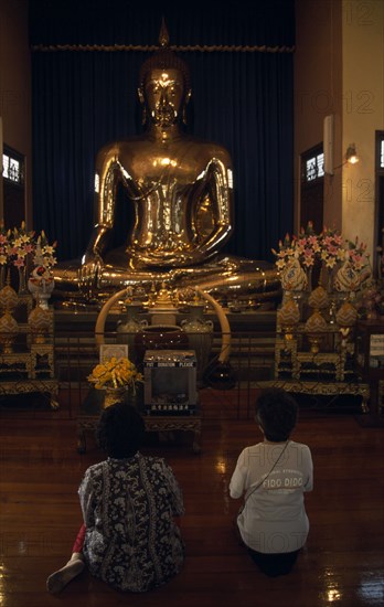 THAILAND, South, Bangkok, Wat Traimit Temple of The Golden Buddha with two women kneeling at prayer in front of the Buddha
