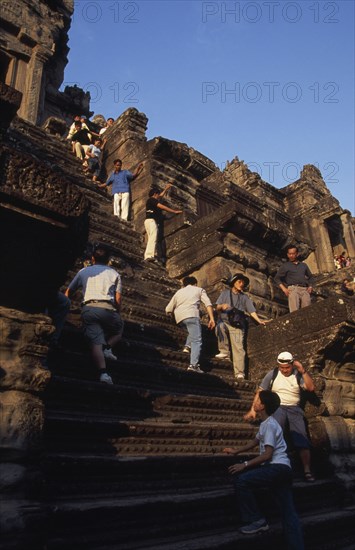 CAMBODIA, Siem Reap Province, Angkor Wat, Tourists climbing steep narrow steps to upper or third level.