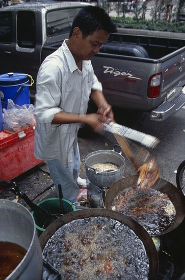 THAILAND, South, Bangkok, Thanon Silom male vendor at his stall on the pavement deep frying fish in woks
