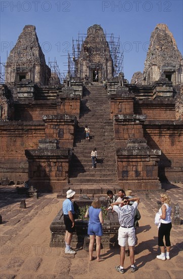 CAMBODIA, Siem Reap Province, Angkor, Preah Rup.  Western tourists with guide at cremation pit in foreground of funereal temple undergoing restoration.