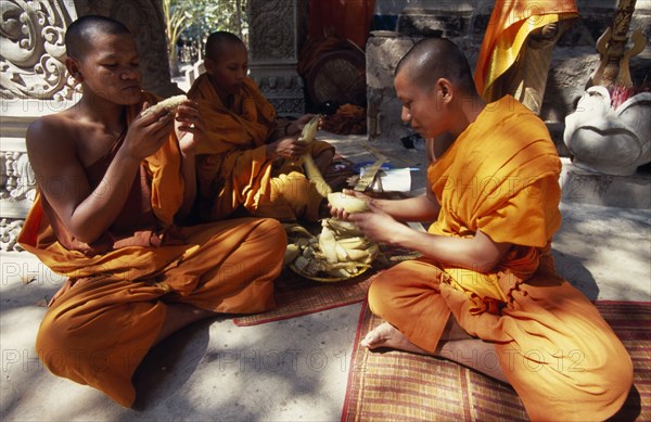 CAMBODIA, Siem Reap Province, Angkor Thom, Buddhist monks eating steamed and boiled corn donated by elderly lady.