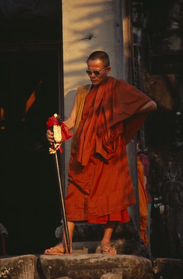 CAMBODIA, Siem Reap, Angkor Wat, Buddhist monk wearing sunglasses and carrying an elaborate walking stick watching the Shaman ceremony