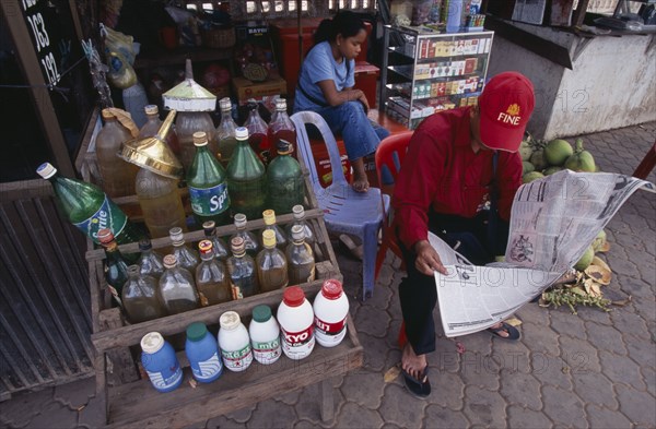 CAMBODIA, Siem Reap, Roadside stall selling bottles of petrol watered down and at the same price as at fuel stations. Man sitting reading a newspaper