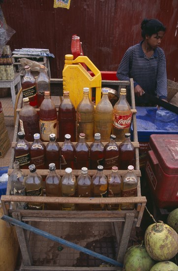 CAMBODIA, Siem Reap, Roadside stall selling bottles of petrol watered down and at the same price as at fuel stations. Woman cutting ice in the background