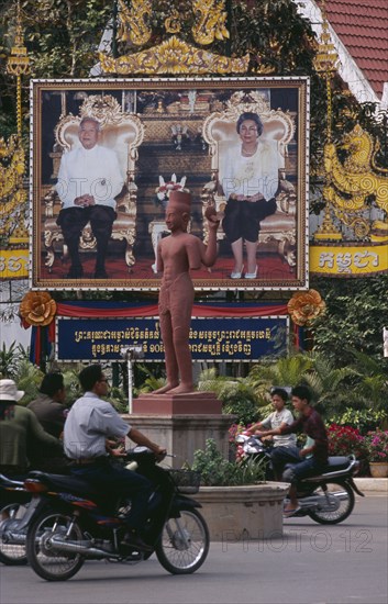 CAMBODIA, Siem Reap, Poster of Sihanouk and his wife by the side of a roundabout with motorbikes going around an armless statue