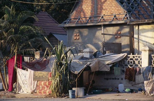 CAMBODIA, Siem Reap, Homeless man washing clothes in a bowl outside his pavement shack