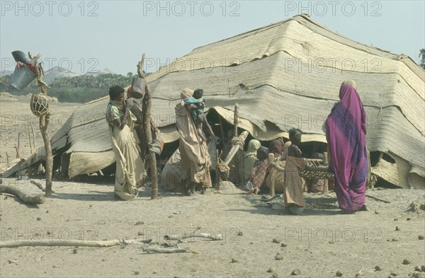 SUDAN, Tribal Peoples, Beja women and children outside tent made from woven palm matting designed to be moveable so as to be able to follow the herds.