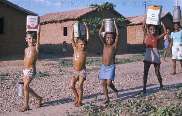 BRAZIL, Teresina, Group of young children of mixed race carrying water in various metal containers on their heads in slum area.