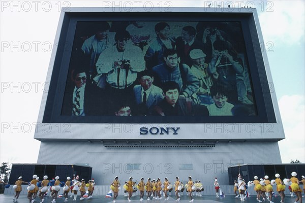 JAPAN, Tokyo, Exhibition of Technology with view of Sony Jumbotron massive Television screen and girls marching with pom poms in foreground.