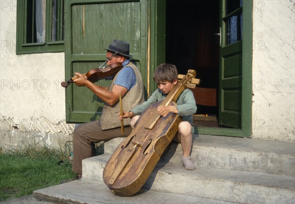 ROMANIA, Transylvania, Gimes Village, "Man and child playing violin and a gardon, a cello like instrument played by hitting the strings with a small stick."