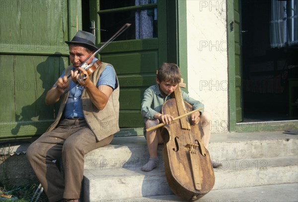 ROMANIA, Transylvania, Gimes Village, "Man and child playing violin and a gardon, a cello like instrument played by hitting the strings with a small stick."