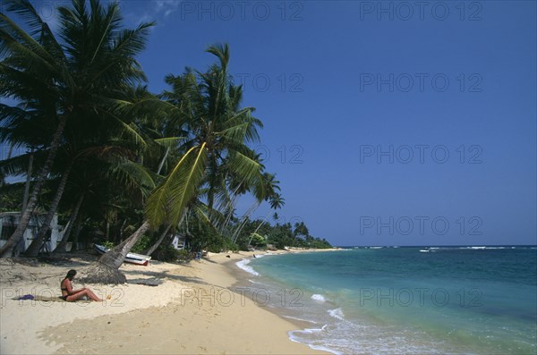 SRI LANKA, Unawatuna, Tourists on narrow strip of sandy beach fringed with palms at popular south coast resort of Unawatuna.