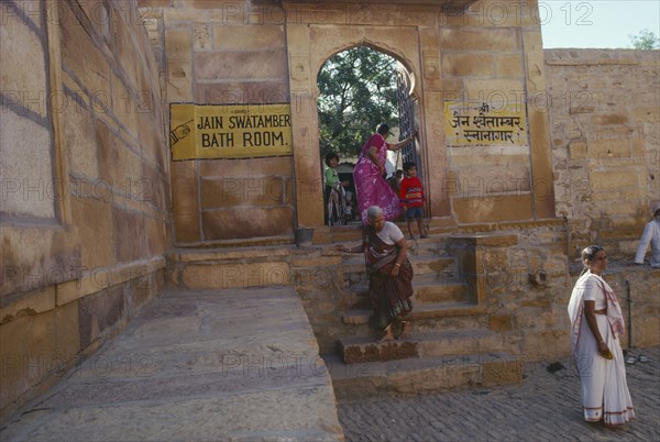 INDIA, Rajasthan, Jaisalmer, Women and children at Jain temple passing sign indicating bath room.  Cult images are washed daily by priests and lay worshippers bath before worship.