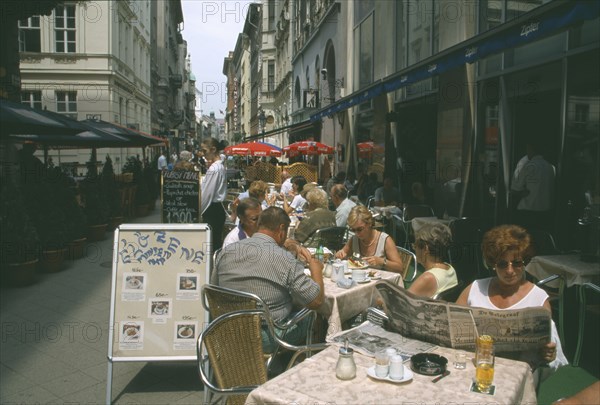 HUNGARY, Budapest, People at outside tables of restaurant with woman reading Hungarian newspaper in the foreground.