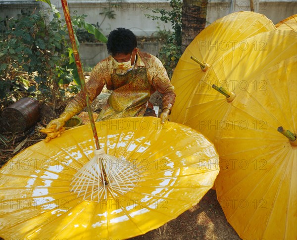 THAILAND, Chiang Mai Province, Bo Sang Village, Man spinning cotton umbrella as he applies colour finnish