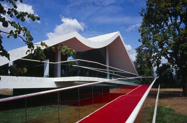 ENGLAND, London, Kensington Gardens.  The Serpentine Gallery Pavilion designed by architect Oscar Niemeyer.  Exterior part framed by trees.