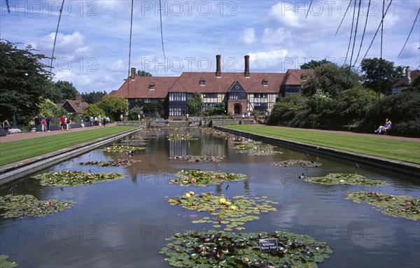 20059213 ENGLAND Surrey Woking Wisley Royal Horticultural Society Garden. View across formal pond with water lilies towards the Tudor style half timbered main entrance building.