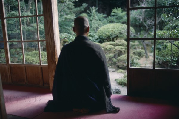 JAPAN, Buddhism, Zen Buddhist monk meditating in front of screen open to garden.