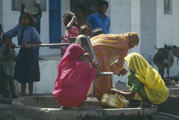 INDIA, Rajasthan, Sisarma, Women and children collecting water from village well and hand pump.
