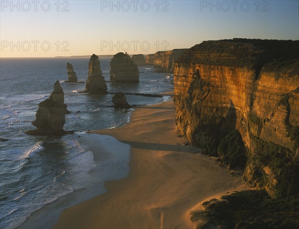 AUSTRALIA, Victoria, Port Campbell N.P, Great Ocean Road. View along the beach and cliffs toward The Twelve Apostles sea stacks in warm evening light
