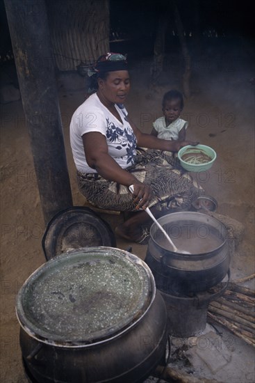 GHANA, Cherepani, Woman cooking over wood burning open topped stove and passing helping of food to small girl sitting beside her.