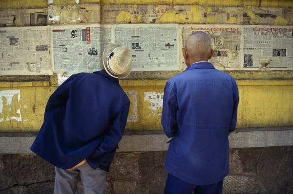 CHINA, Yunnan Province, Kunming, Two men reading newspapers displayed on wall.