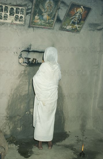 INDIA, West Bengal, Sundarbans, Elderly woman doing her evening puja in mud hut.