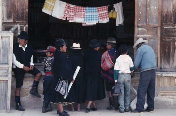 ECUADOR, Loja, Saraguro, Customers in mix of traditional and westernised dress outside shopfront.