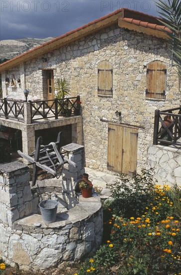 CYPRUS, Lineia, Stone house with overhanging tiled roof and wooden window shutters and door with well in courtyard in the foreground.