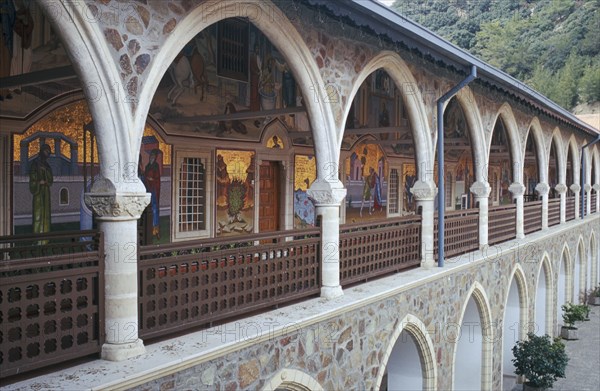 CYPRUS, Troodos Mountains, Kykko Monastery, Tourist visitors in courtyard of monastery with religious mosaics decorating length of wall of first floor arcade seen on left.