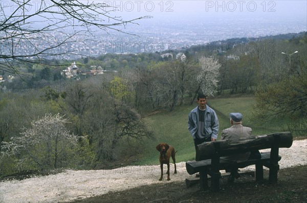 HUNGARY, Budapest, Dog walkers in conversation in park above city.