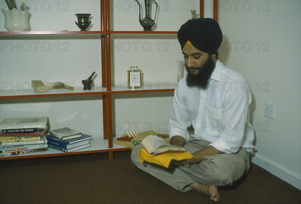 ENGLAND, Religion, Skihism, Sikh man sitting on the floor of his home reading Gutka an abbreviated version of the Guru Granth Sahib Scripture.