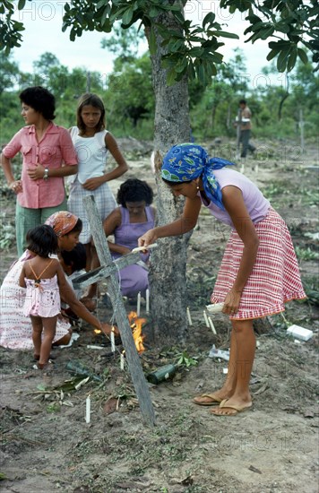 BRAZIL, Sao Paulo, Ribeirao Bonito, Catholic family conducting memorial service around makeshift grave in slum area graveyard.