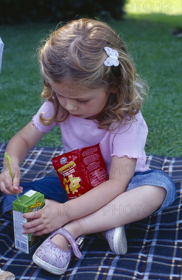 ENGLAND, West Sussex, Chichester, The Bishops Palace Gardens.  Girl aged three putting straw into carton of low sugar blackcurrant juice drink during picnic lunch.