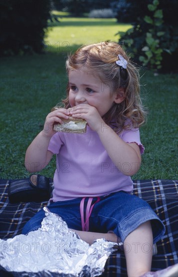 ENGLAND, West Sussex, Chichester, The Bishops Palace Gardens.  Girl aged three eating brown bread and lettuce sandwich during picnic lunch.