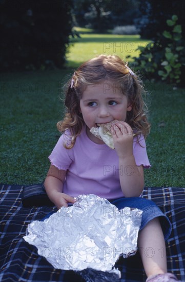 ENGLAND, West Sussex, Chichester, The Bishops Palace Gardens.  Girl aged three eating brown bread and lettuce sandwich during picnic lunch.